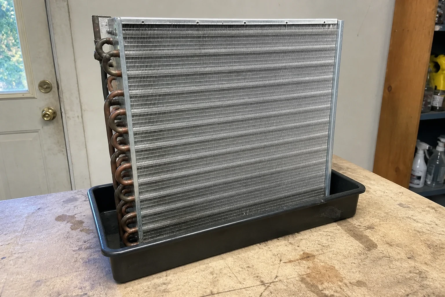 Detached finned cooling coil with copper return bends standing in a shallow tray.